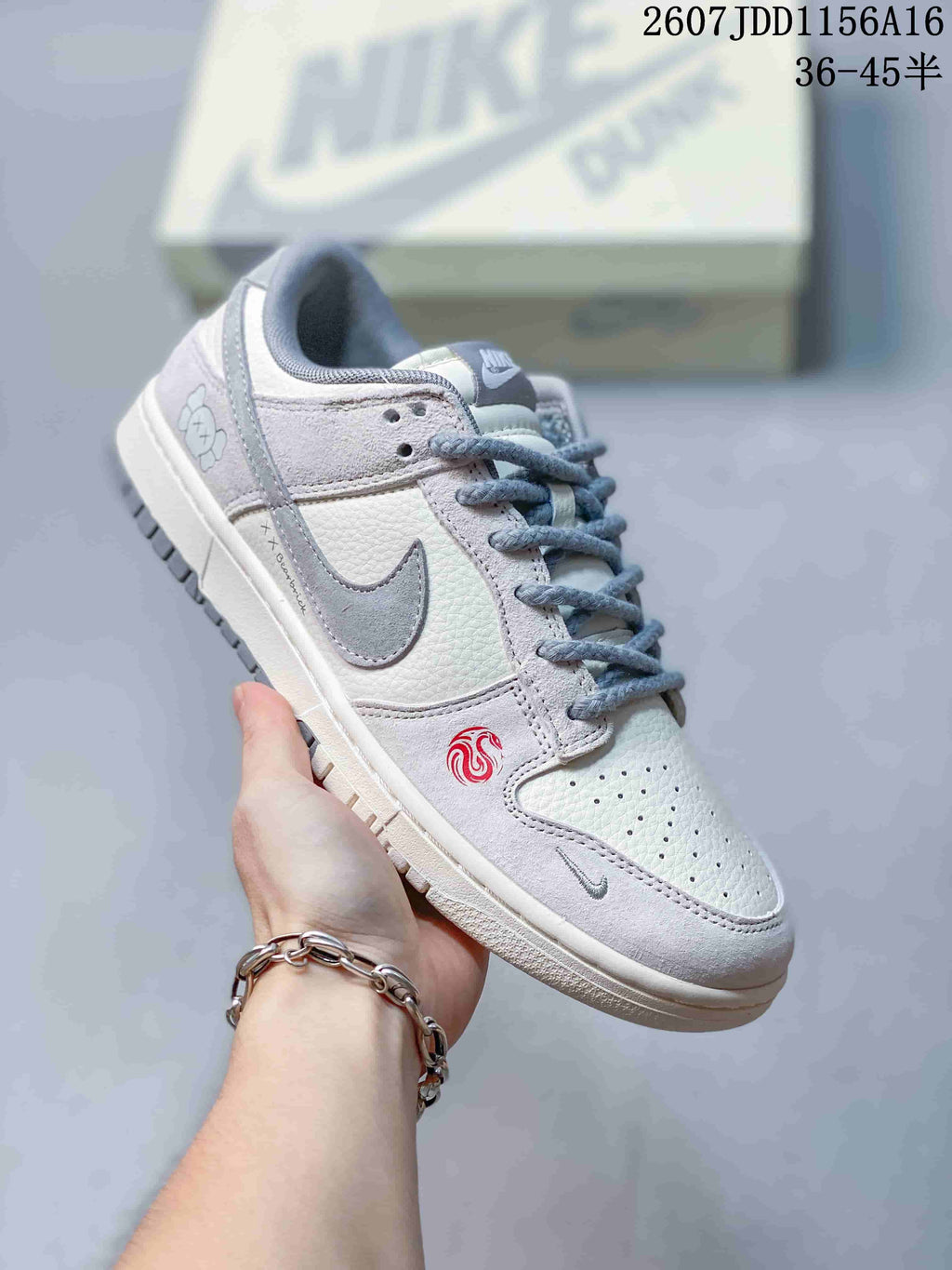 Close side view of an off-white and grey sneaker with grey-blue laces, contrasting Swoosh and a red forefoot emblem.