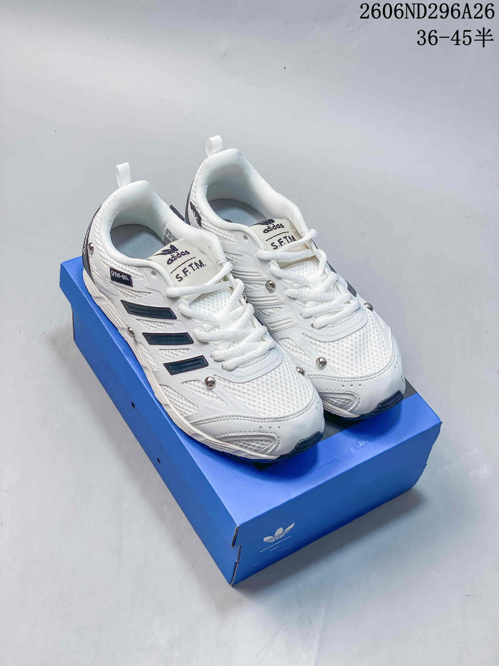 Pair of white Adidas Originals PR SFTM low-top sneakers displayed on a blue shoebox, with the advertised size range visible at the upper right.