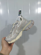 Hand-held side view of eggshell and silver mesh sneakers with gray overlays and cream sole accents.