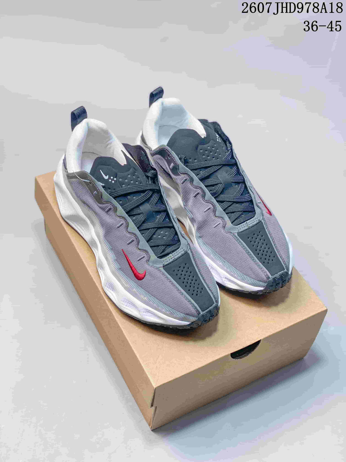 Pair of gray, white, and red Nike sneakers displayed on a shoebox, with style code and size range text visible above.