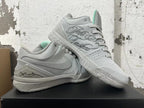 Pair of light grey basketball shoes shown together, with Swoosh branding, signature details, and teal tongue accents.