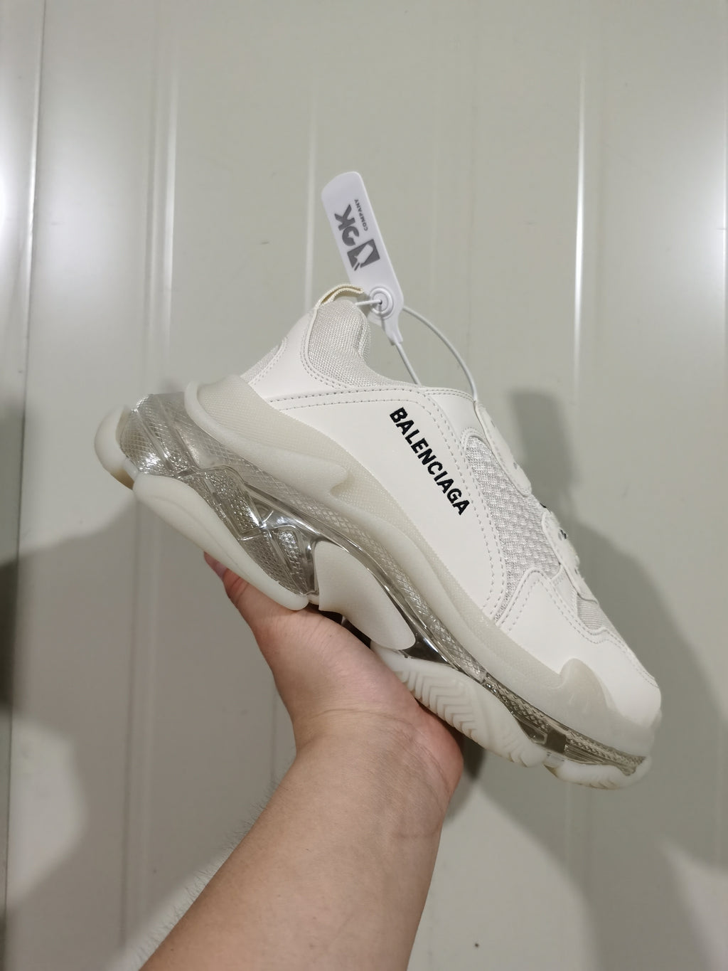 Side view of a white Balenciaga sneaker with black side branding and a clear-look layered sole.