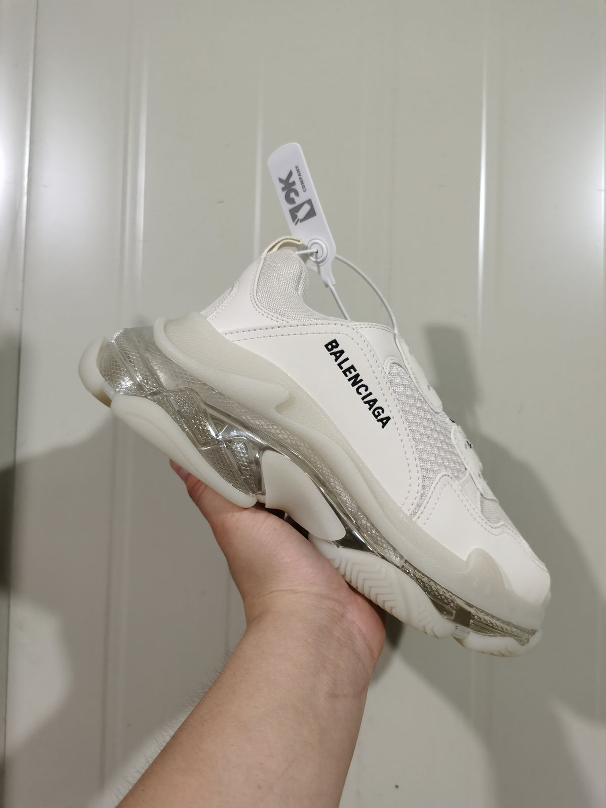 Side view of a white Balenciaga sneaker with black side branding and a clear-look layered sole.
