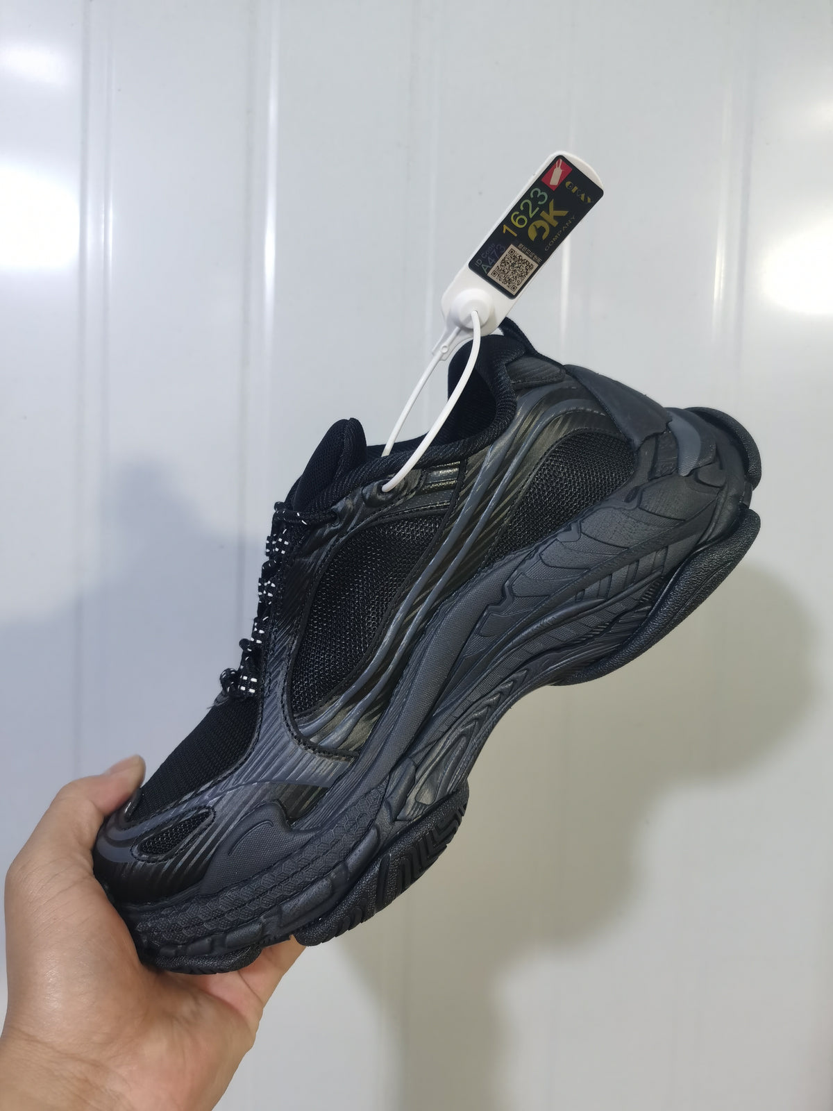 Black and dark grey Balenciaga Triple S 2 sneaker shown from a side angle with layered panels, mesh sections and a chunky sole.