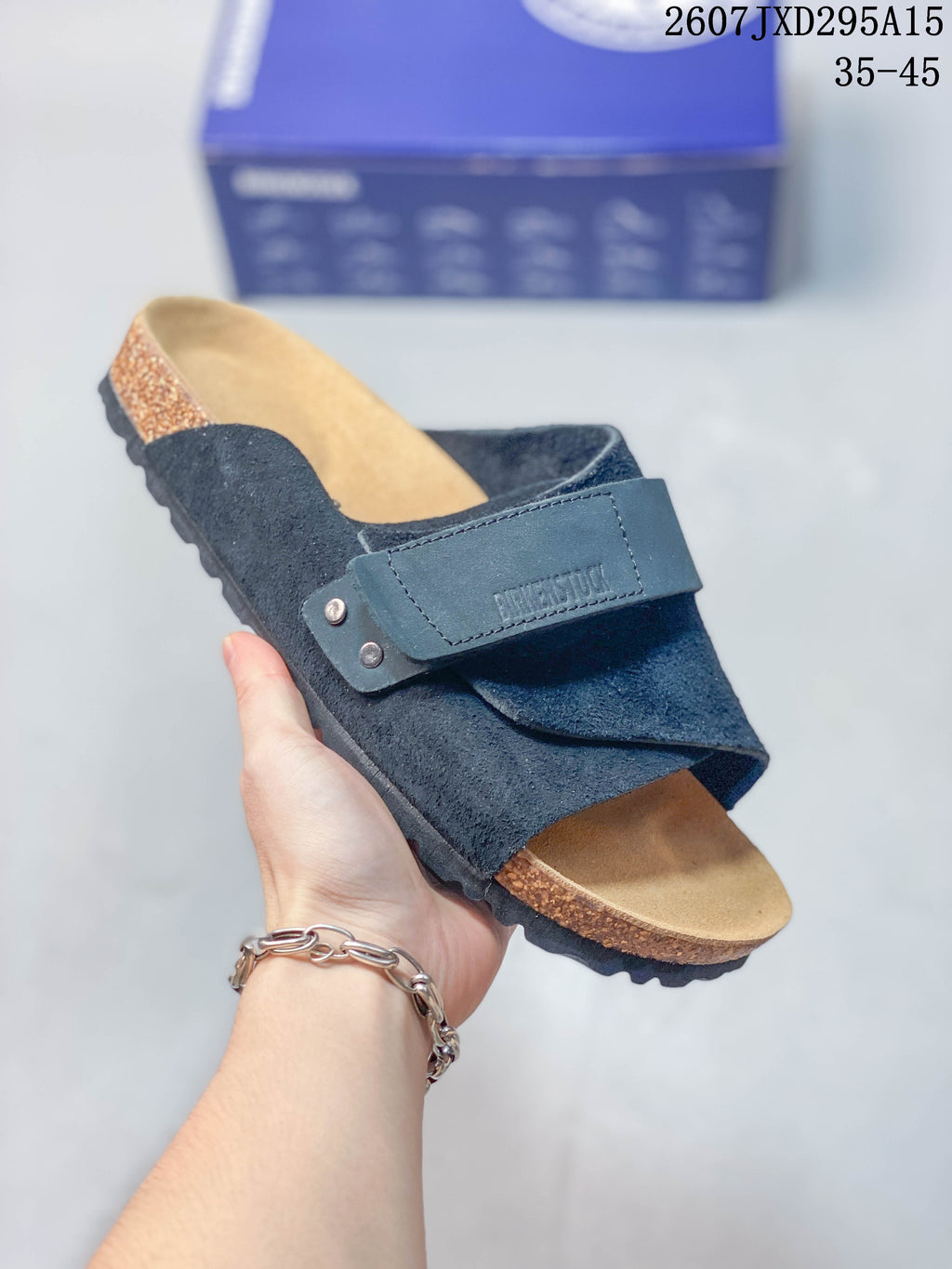 Angled close view of the dark crossover sandal, adjustable strap, suede-look upper and cork-look footbed edge.