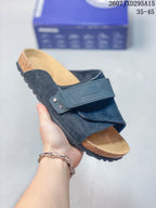 Angled close view of the dark crossover sandal, adjustable strap, suede-look upper and cork-look footbed edge.