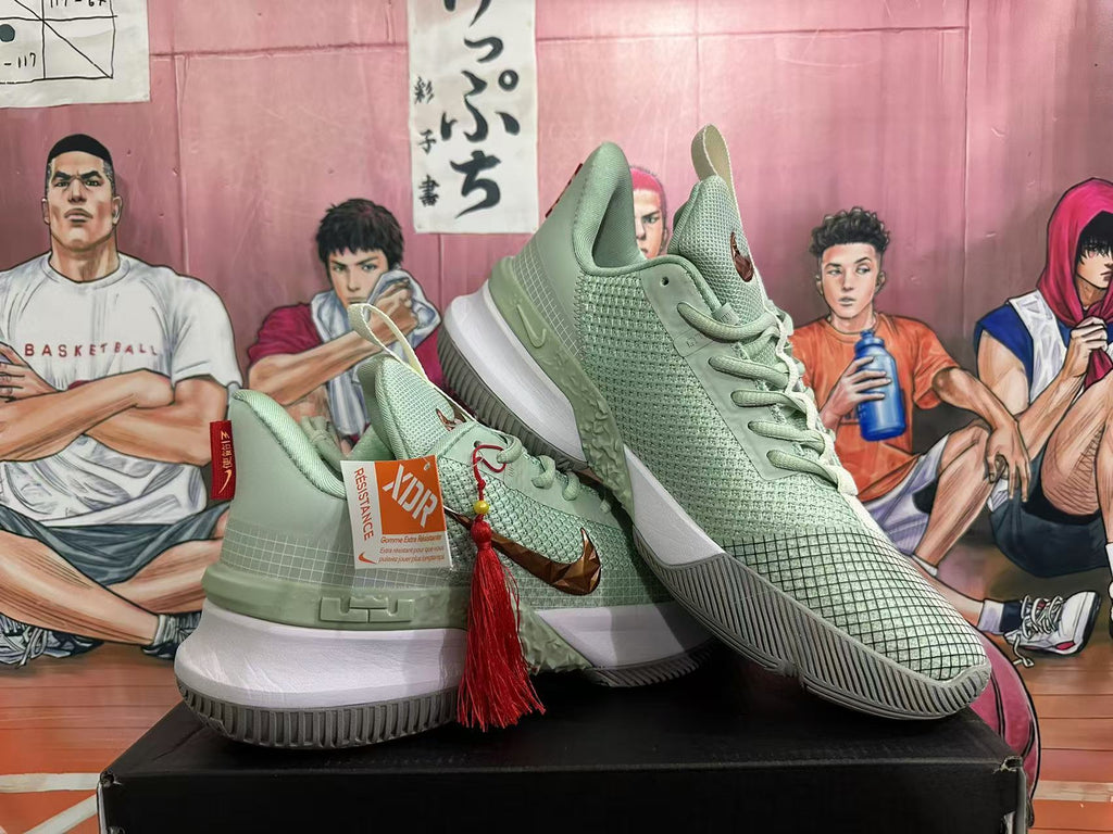 Angled product view showing the jade green Nike sneaker pair, bronze-toned side detailing, white midsoles, and decorative red tassel.