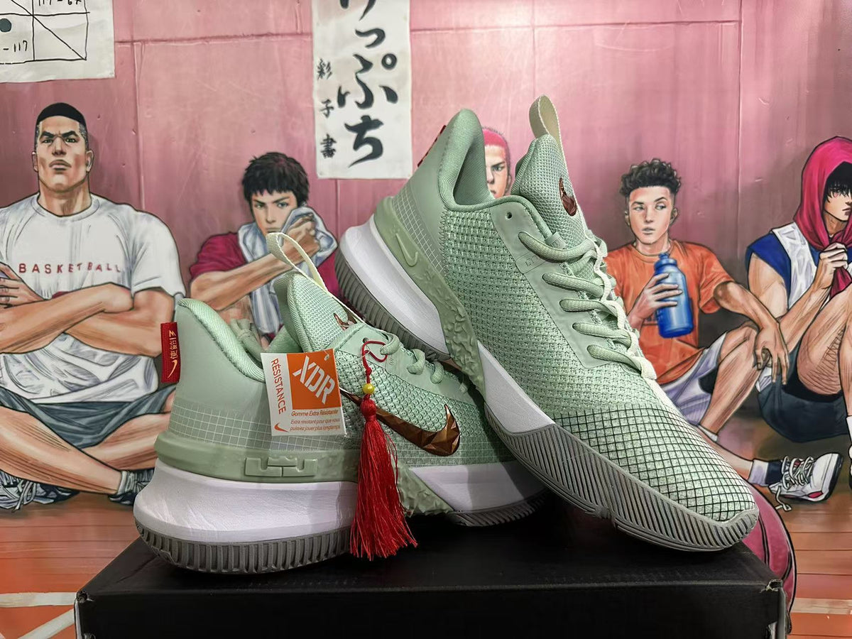 Angled product view showing the jade green Nike sneaker pair, bronze-toned side detailing, white midsoles, and decorative red tassel.