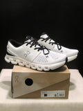 Pair of Ivory and Black On Cloud X4 sneakers displayed on their shoe box.