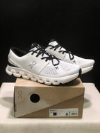 Pair of Ivory and Black On Cloud X4 sneakers displayed on their shoe box.