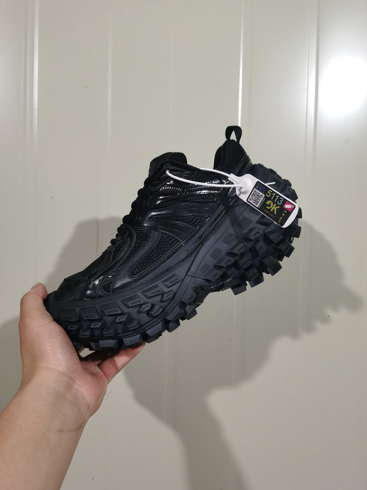 Black sneaker shown from the opposite side with a hang tag attached near the collar.