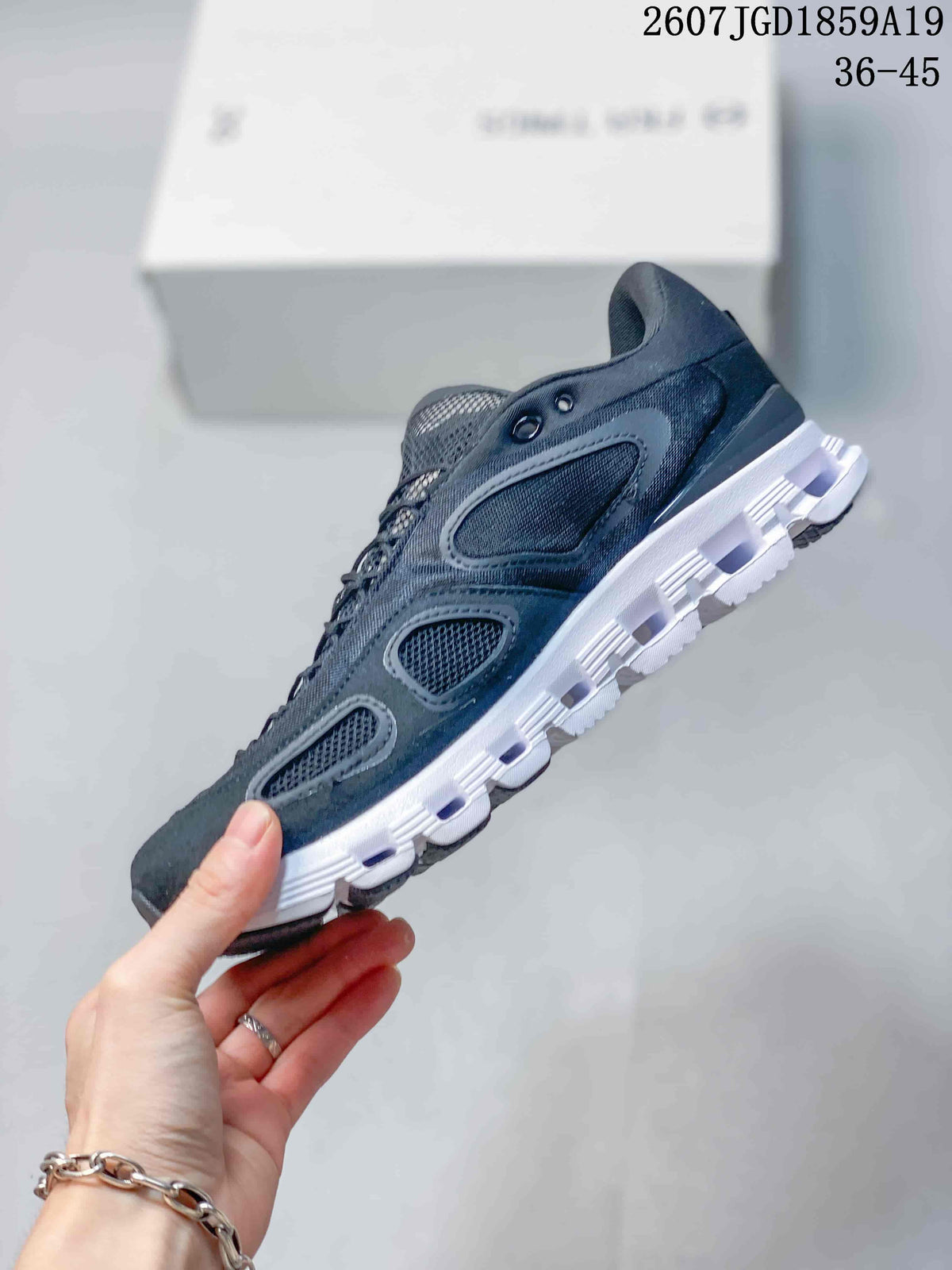 Side profile of a black On sneaker showing layered mesh panels, oval side details, laces, and a white segmented sole.