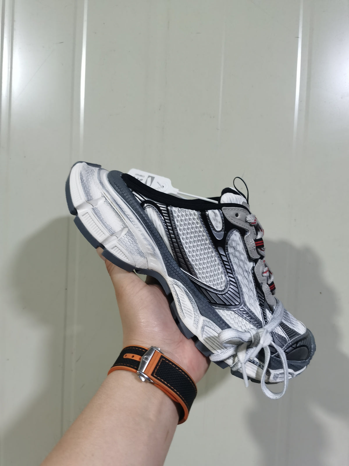 Close-up side view of a grey, white and black 3XL sneaker with layered panels, textured mesh and red lace-area detailing.