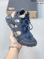 Angled side view of the black sandal showing the branded strap, open side construction, adjustable fastening system, and textured outsole.