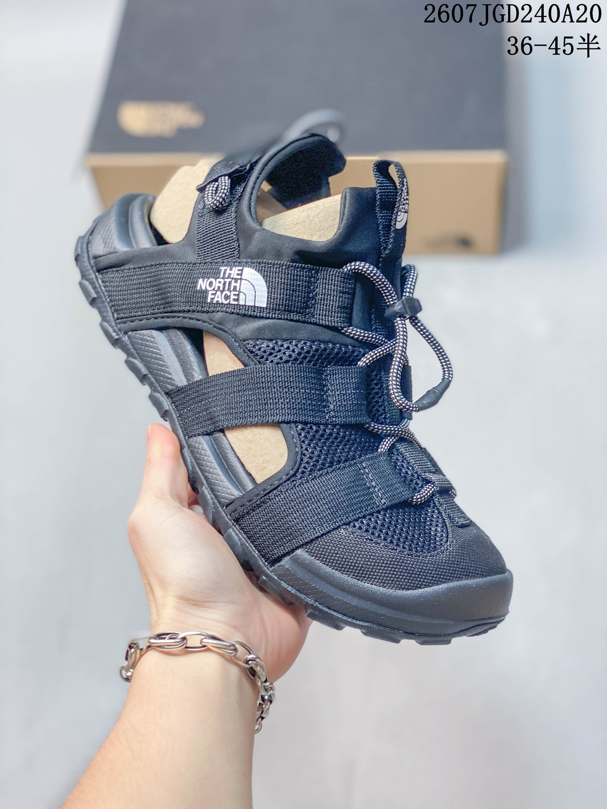 Angled side view of the black sandal showing the branded strap, open side construction, adjustable fastening system, and textured outsole.