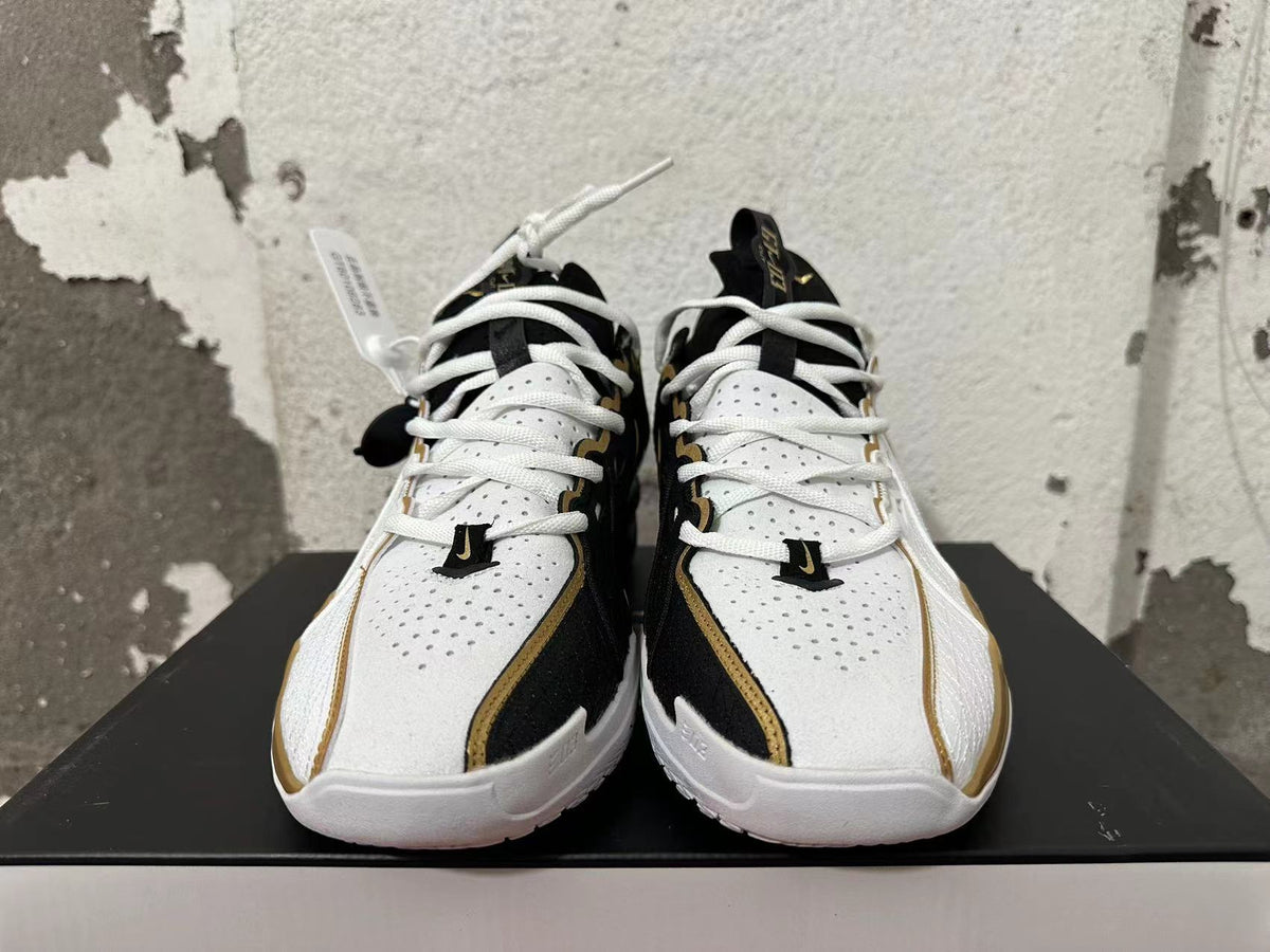 Front view of white-and-black Nike basketball shoes with white laces and gold trim.