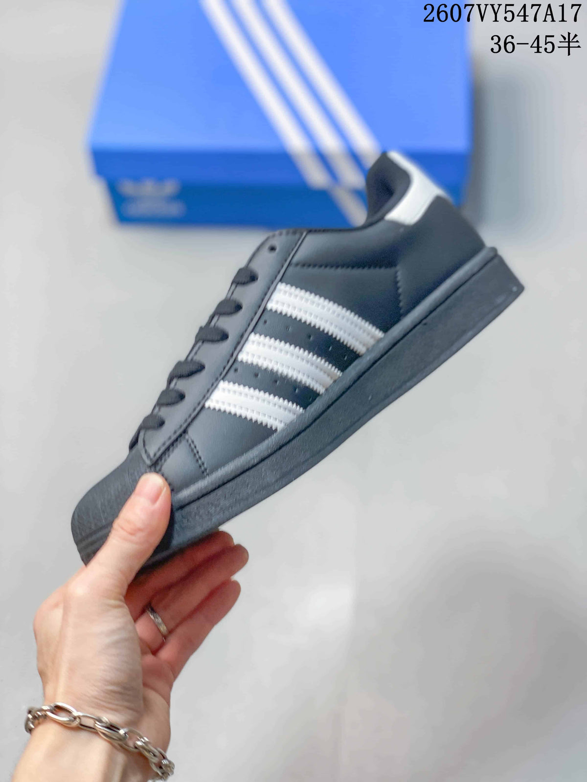 Side profile of a black Adidas Superstar sneaker showing three white stripes, a low-top shape, and a dark sole.