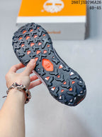 Close view of the dark lugged outsole with orange openings and a Timberland tree emblem.