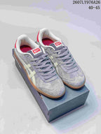 Pair of gray Onitsuka Tiger Tokuten sneakers with cream side stripes, red heel accents, and an amber outsole displayed on a shoebox; image text shows style code 2607LY976A26 and size range 40–45.