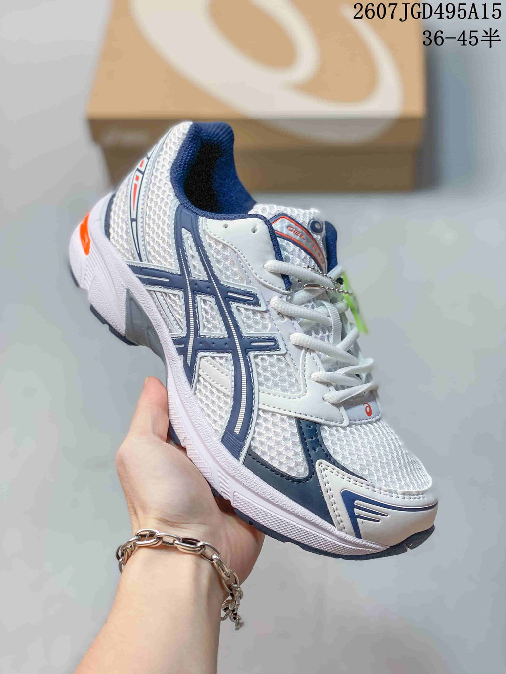 Angled side view of the white ASICS GEL-1130 sneaker showing its layered upper, navy branding details and orange heel accent.