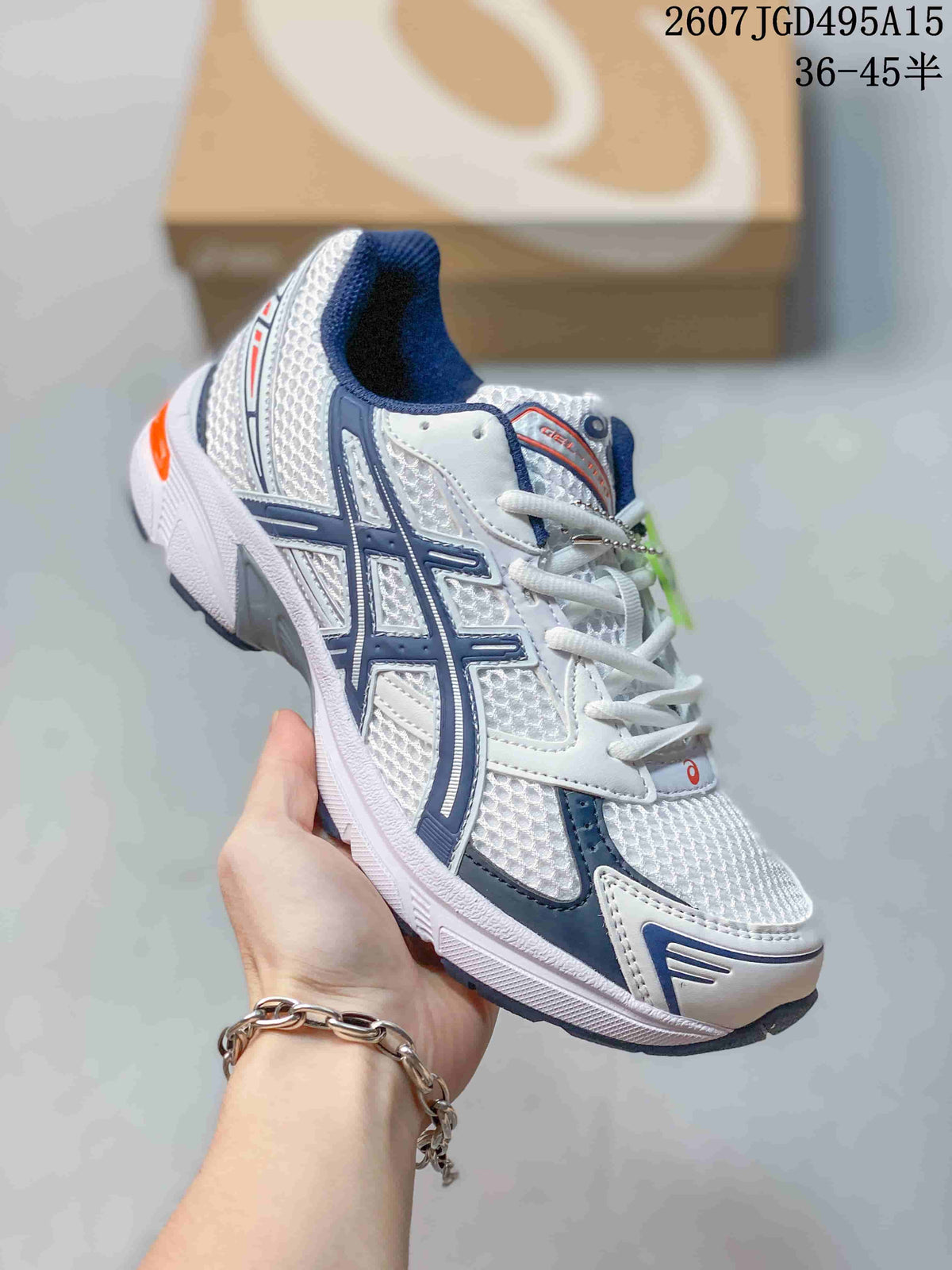 Angled side view of the white ASICS GEL-1130 sneaker showing its layered upper, navy branding details and orange heel accent.