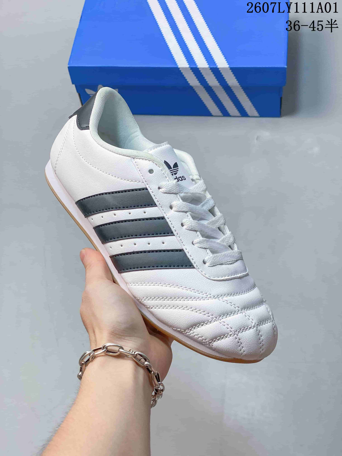 White Adidas Taekwondo low-top lace-up sneaker with dark stripes.