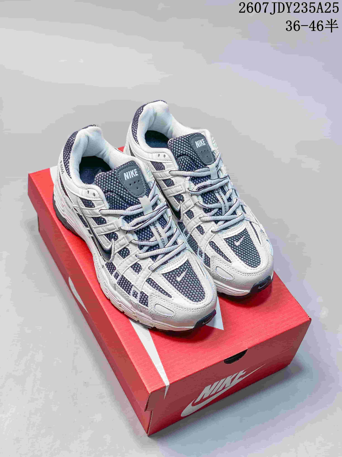 White Nike P-6000 sneakers with dark blue-gray mesh displayed on a red shoebox.