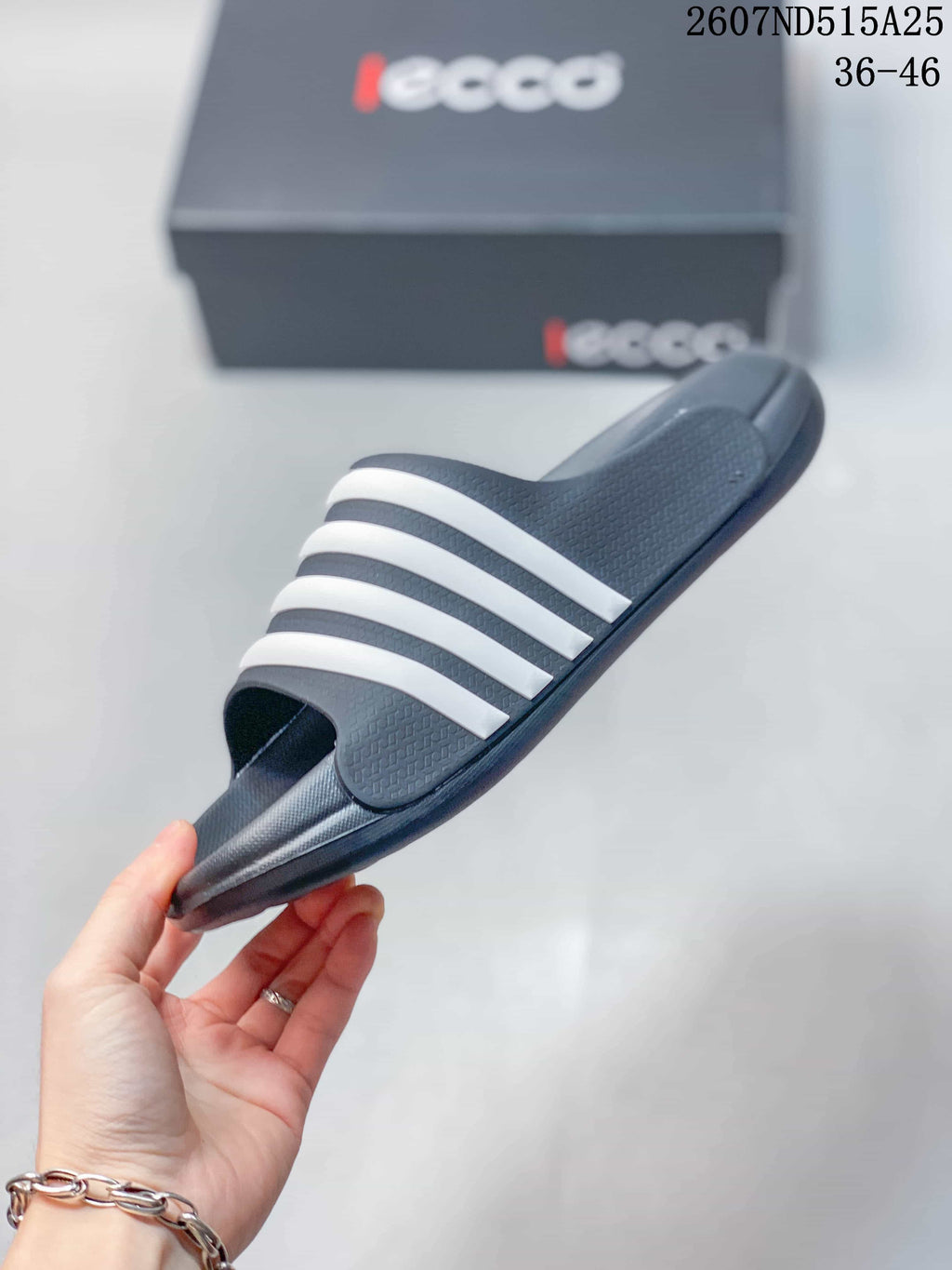 Side view of a dark slide sandal with four white bands, a raised footbed, and a molded outsole.