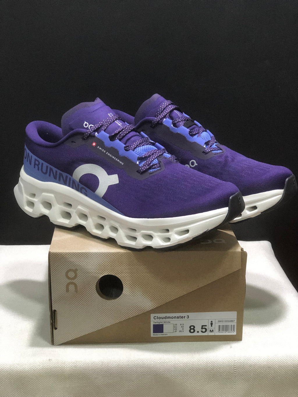 Purple and blue On Cloudmonster 3 running shoes displayed on their shoe box, with the box label visible.