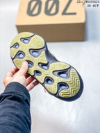 Underside view showing the sneakers' pale yellow-green and black outsole with repeating zigzag tread sections.