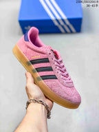 Angled side view showing the pink Adidas Gazelle sneaker, black stripes, gum-colored sole and visible Gazelle side text.