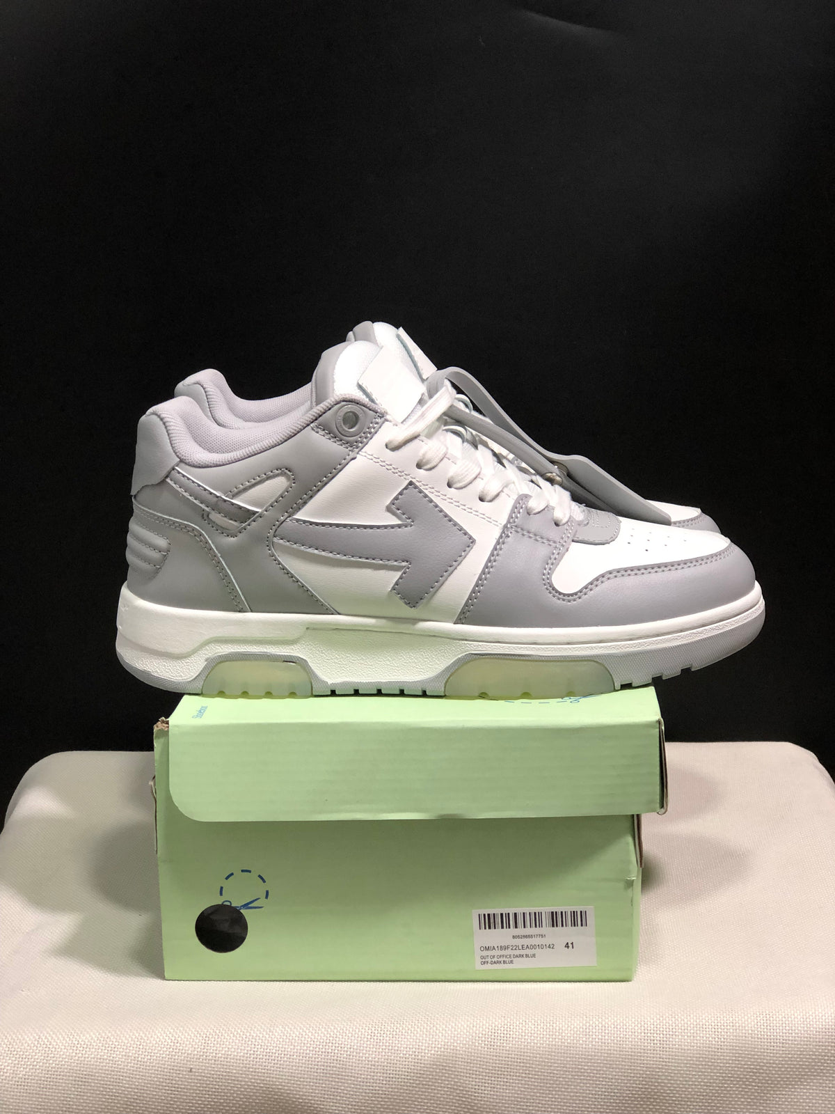 Side profile of the white and gray sneakers showing layered panels, padded collar, and chunky outsole.