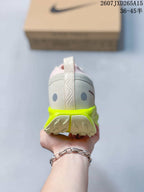 Rear view of the sneaker showing the heel pull tab, light gray textile upper, pink lining, and neon yellow outsole edge.