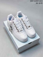 Pair of white Nike Air Force 1 '07 low-top sneakers displayed on a shoe box with spare accessories visible.