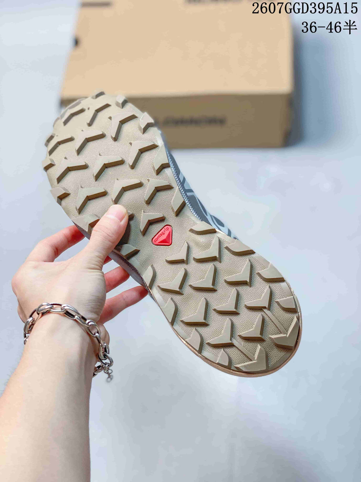 Underside of the shoe showing a beige outsole with deep directional lugs and a red Salomon mark.