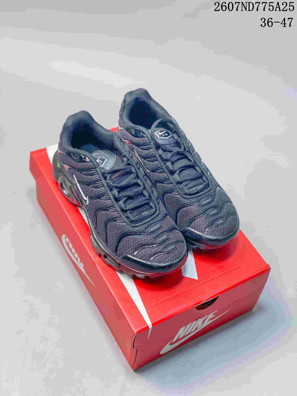 Pair of black Nike Air Max Plus TN sneakers displayed on a red Nike shoe box; visible text shows 2607ND775A25 and 36–47.