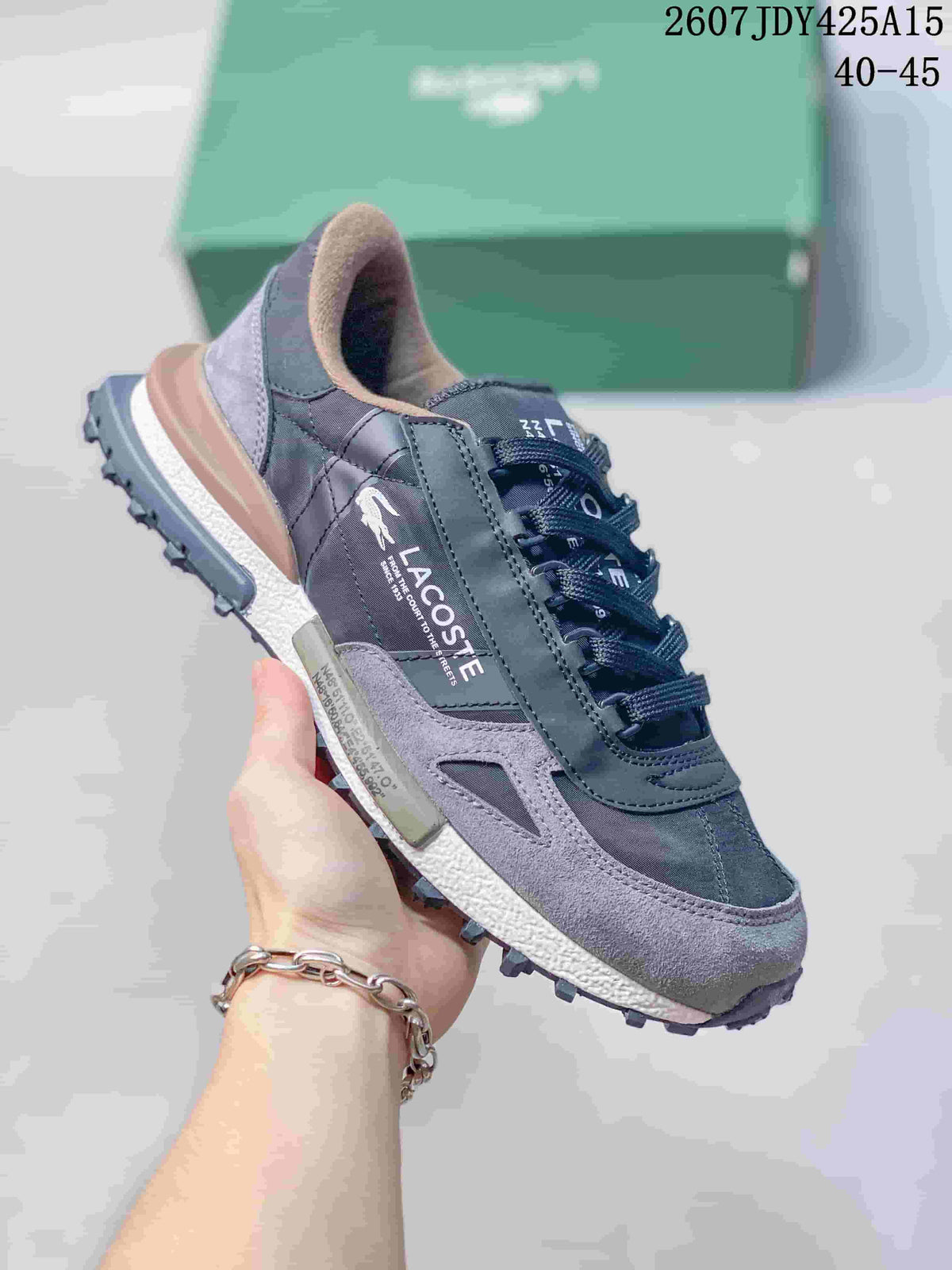 Angled side view of a gray Lacoste sneaker with visible crocodile logo, layered panels, and lugged outsole.