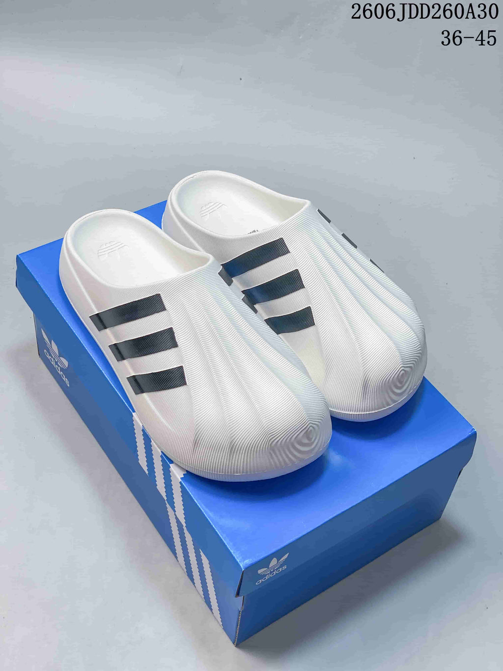 White adidas Originals adiFOM Superstar mule with dark side stripes, shown on a blue shoebox.