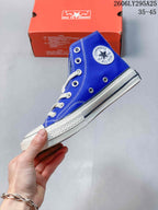 Side view of the blue high-top sneaker showing the circular ankle patch, white stitching, metal eyelets and striped rubber sidewall.