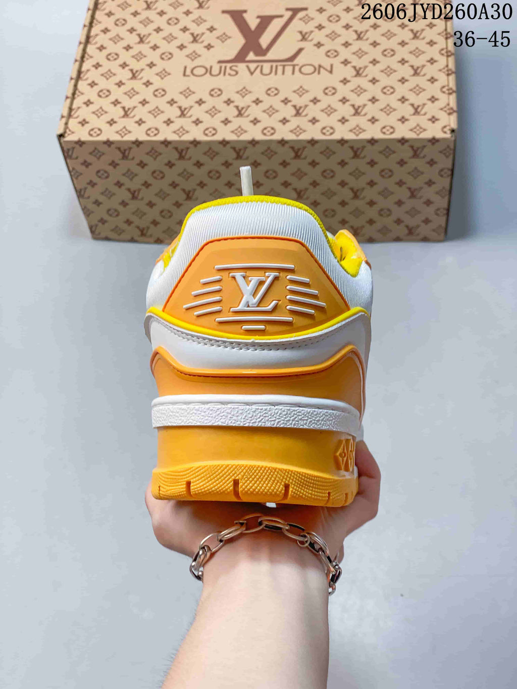 Rear view of a white Trainer Maxi sneaker showing its orange heel panel and yellow outsole.