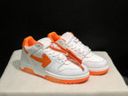 Front three-quarter view of the white and orange sneaker pair with laces and contrasting outsole details.