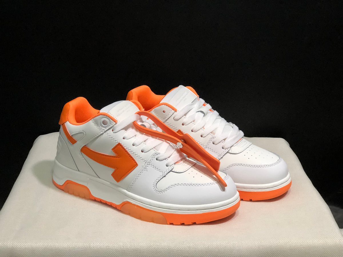 Front three-quarter view of the white and orange sneaker pair with laces and contrasting outsole details.