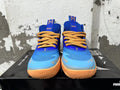 Front view of blue and light blue Puma Melo basketball shoes with yellow-orange laces and sole accents.