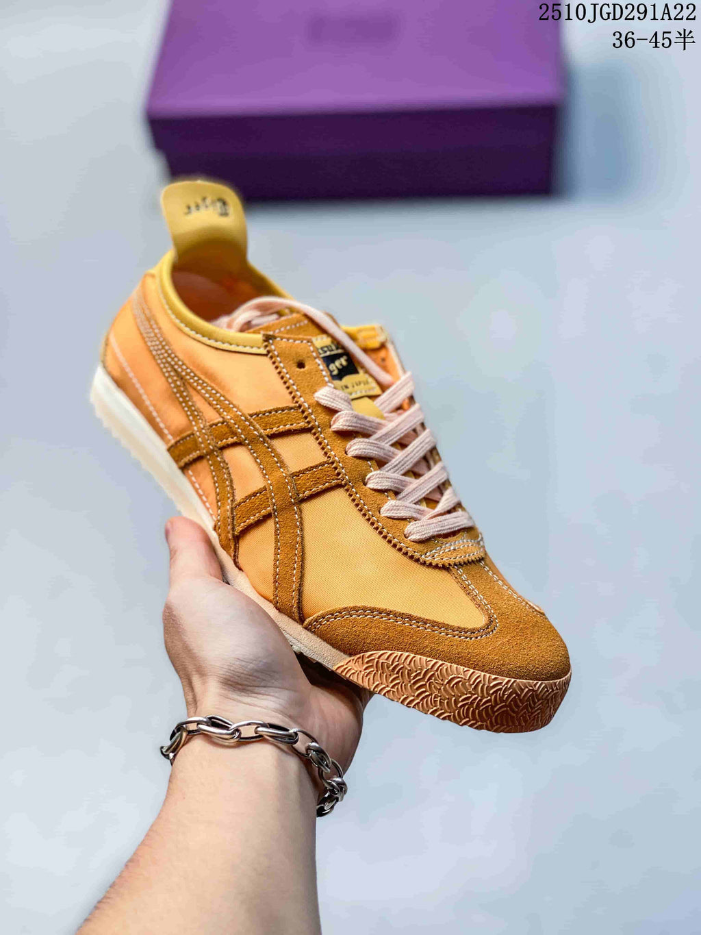 Orange and tan Onitsuka Tiger sneaker held in hand, showing contrast stripes, stitched overlays and a textured rubber outsole.