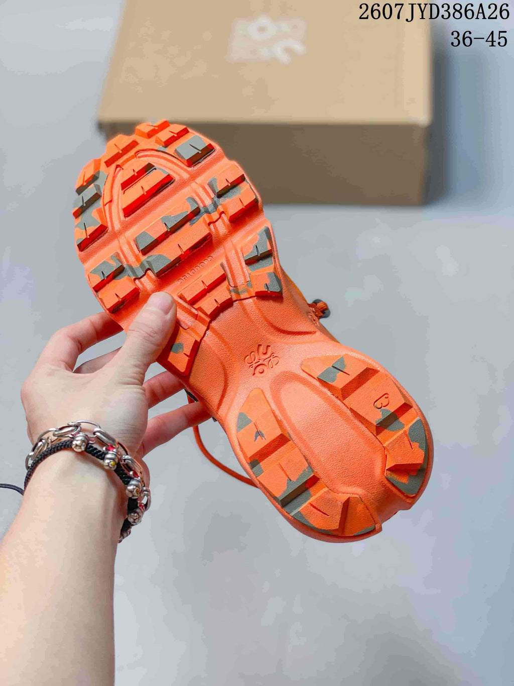Underside view of an orange sneaker showing the sculpted outsole, traction elements, and open cushioning channels; the JYD386A26 code and 36–45 range are visible.