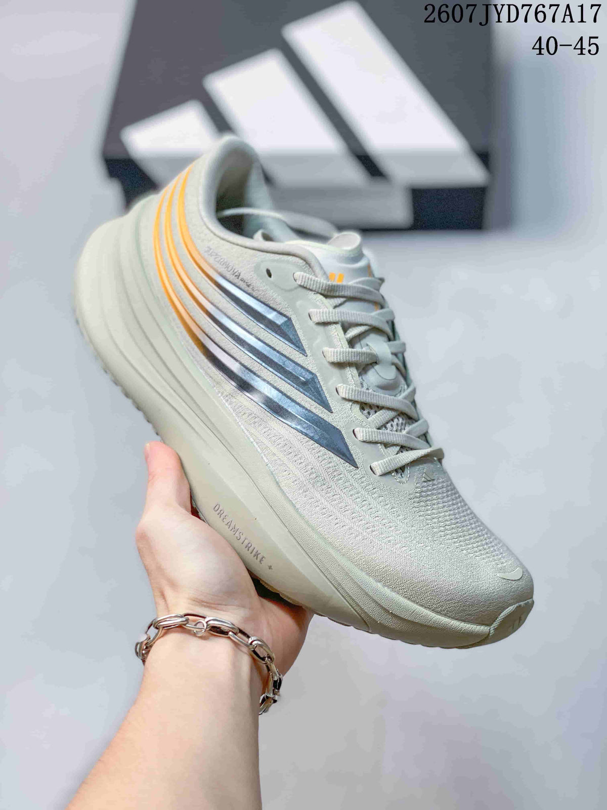 Close side view of a light gray Adidas sneaker with orange and dark layered accents.