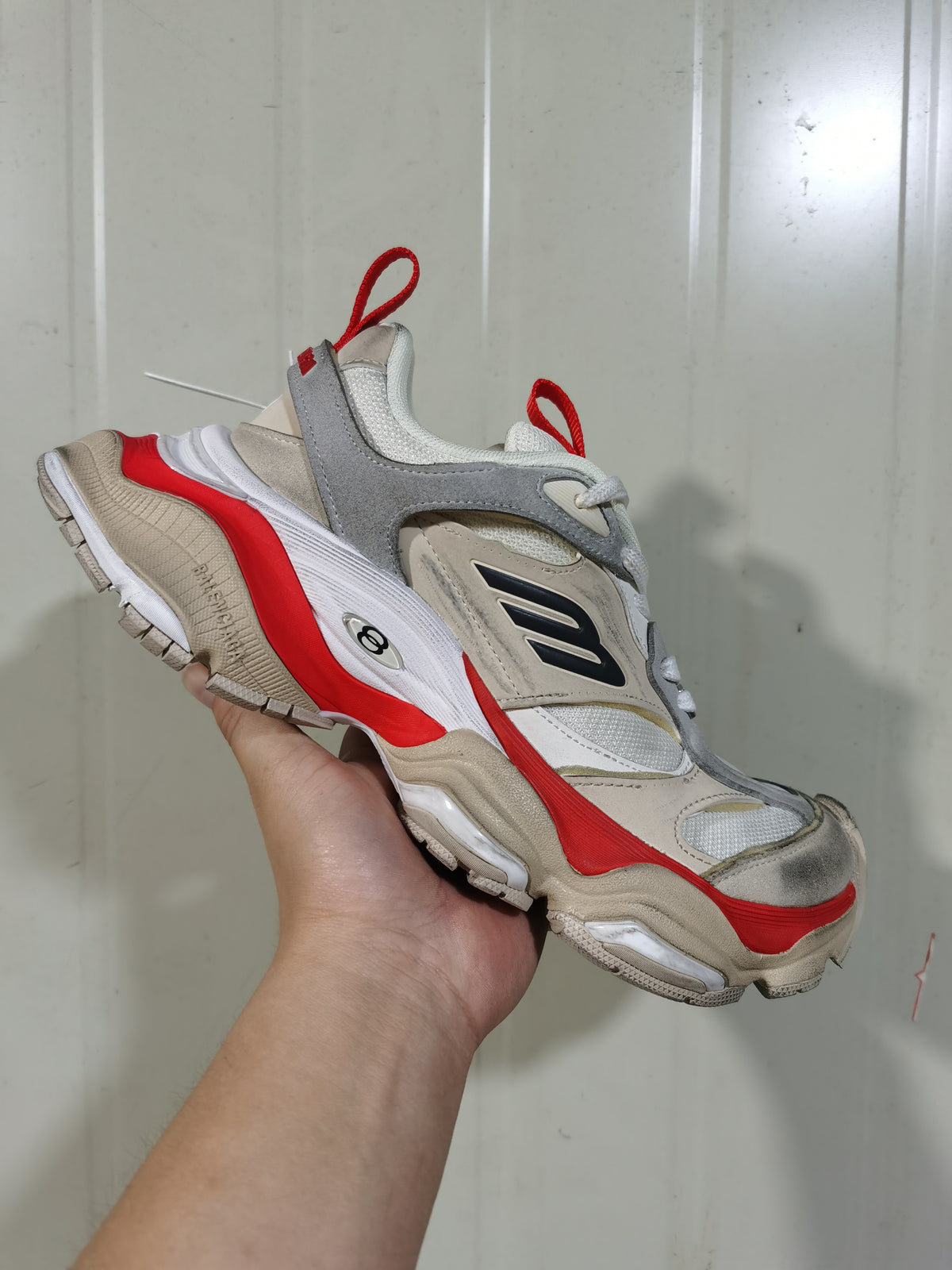 Front three-quarter view of the sneaker highlighting the mesh toe area, layered panels, red-orange accents and segmented outsole.
