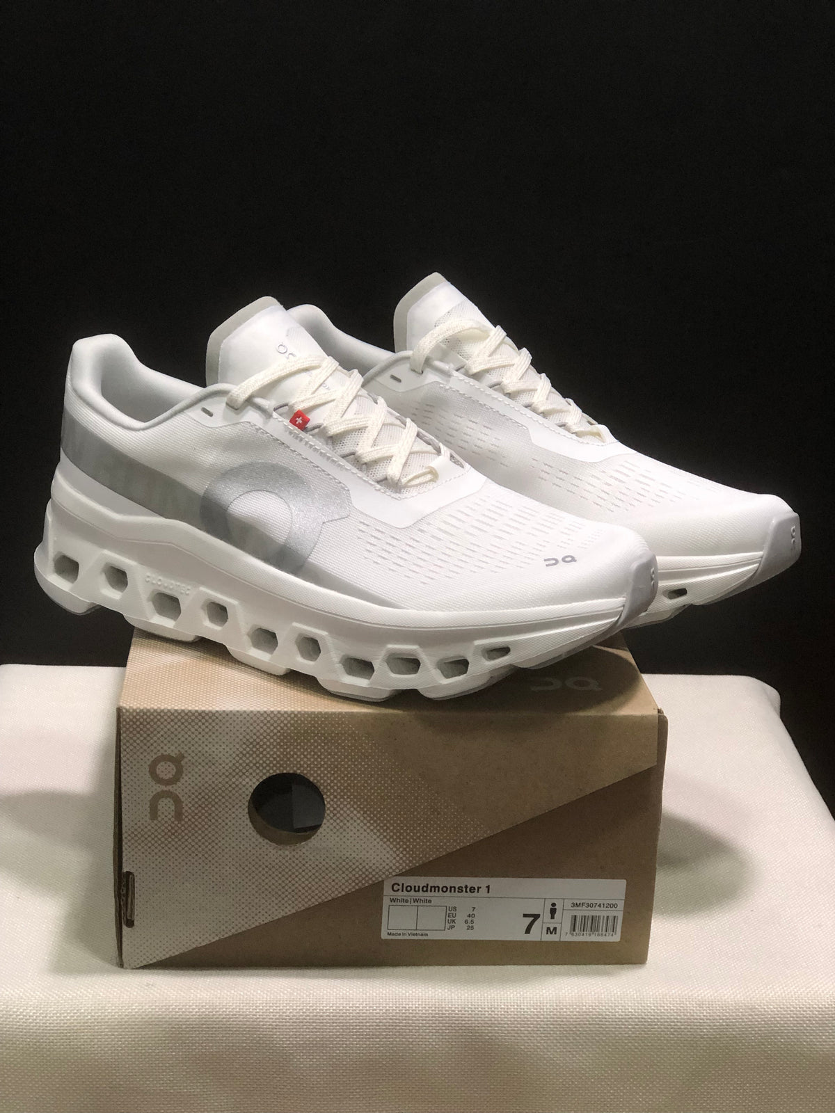 White On Cloudmonster 1 sneakers displayed on a branded shoe box in a three-quarter view.