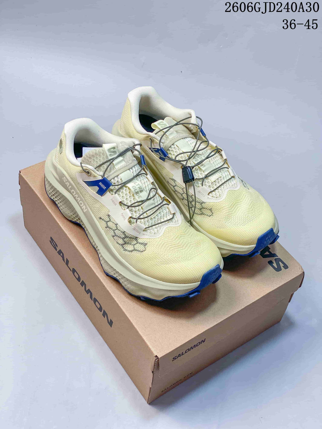 Pair of pale cream Salomon Ultra Glide 4 trail running shoes with blue outsole accents, shown on a shoebox.