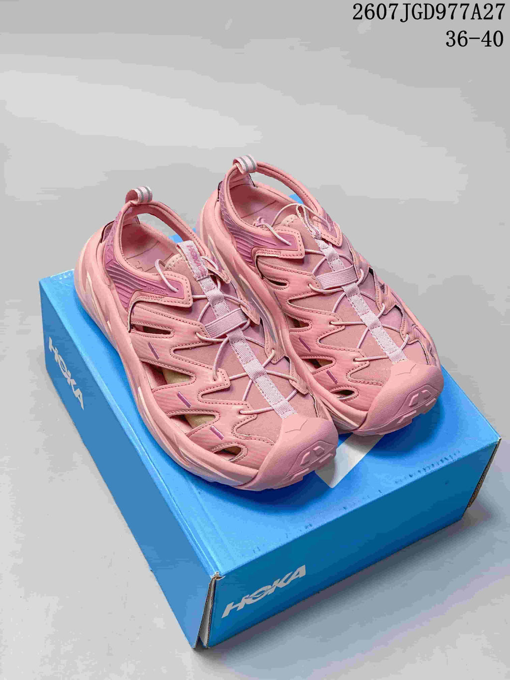 Pair of pink HOKA Hopara OG sandals displayed on a blue shoe box; overlay shows code 2607TGD977A27 and size range 36–40.